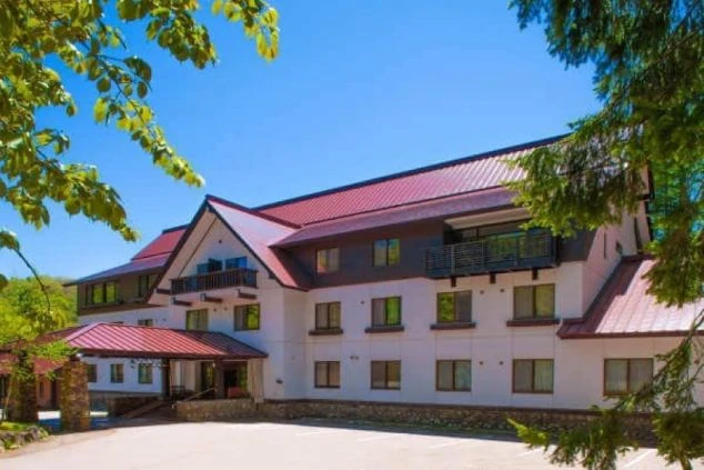 赤色の屋根と白い壁が特徴的な、森の中に佇む飛騨高山のペットと泊まれるホテルの外観の画像。周囲は緑豊かな木々に囲まれており、自然に囲まれたリゾートホテルでのリゾートバイトが体験できます。