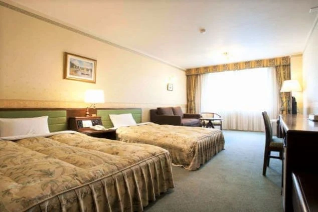 ツインベッドが置かれた飛騨高山のペットと泊まれるホテル客室の画像。窓からは明るい光が差し込み、ソファや机も備え付けられています。