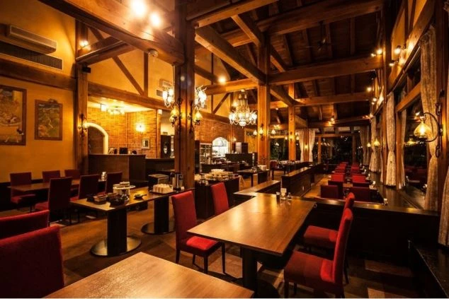 温かい照明に照らされた、広々とした飛騨高山のレストランの店内の画像。木製の梁とレンガの壁が特徴的で、赤い椅子がアクセントになっています。リゾートバイトでのレストラン業務のイメージ