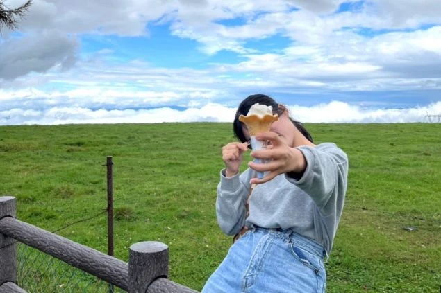 標高の高い牧場で、雲海をバックに濃厚なソフトクリームを味わう女性の画像。大自然の中で働きながら、旅気分を満喫できる住み込みバイトの魅力。