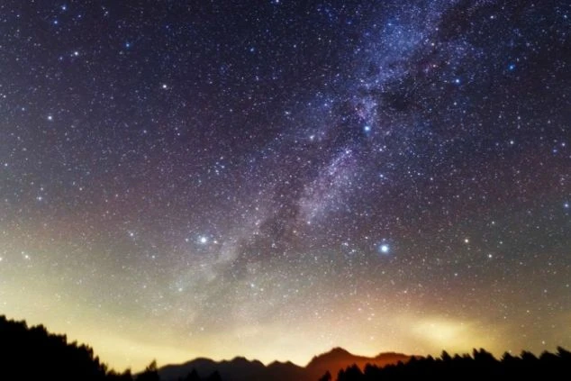 満天の星空に天の川が広がる夜空の画像。地平線近くには山々のシルエットが見え、リゾートバイトで都会を離れて体験できる、非日常的な美しい星空。