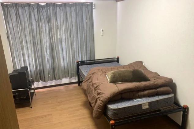 リゾートバイトの個室寮の室内。シングルベッドとテレビが備え付けられたプライベート空間の寮画像。