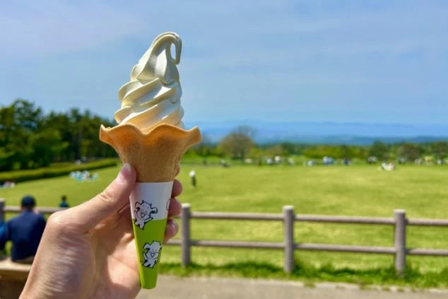岡山県の大山まきばみるくの里で、青空の下、ソフトクリームを持つ手の画像。