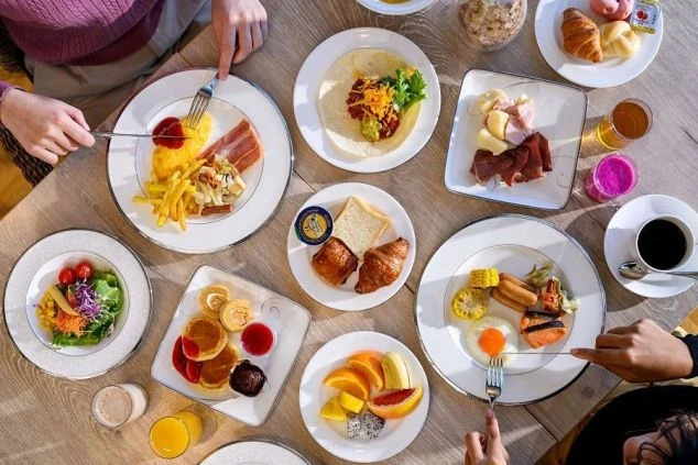 朝食ビュッフェのテーブルに並べられた、洋食とフルーツなど彩り豊かな料理。リゾートバイトのまかないが充実していることを示し、ホテルや旅館の調理補助、レストランスタッフの求人に興味がある方に訴求する画像。