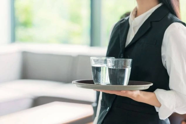 ホテルのレストランでトレイに水が入ったグラスを運ぶホールスタッフ。リゾートバイトで配膳や接客業務に携わりたい方へ、仕事内容をイメージさせる画像。