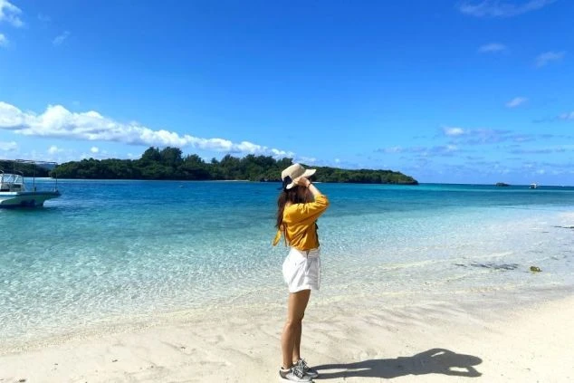 沖縄の透明度の高いエメラルドグリーンのビーチで、海を眺める女性の後ろ姿。リゾートバイトの休日を満喫したい方や、海が好きで沖縄での住み込みバイトを探している方に最適な画像。