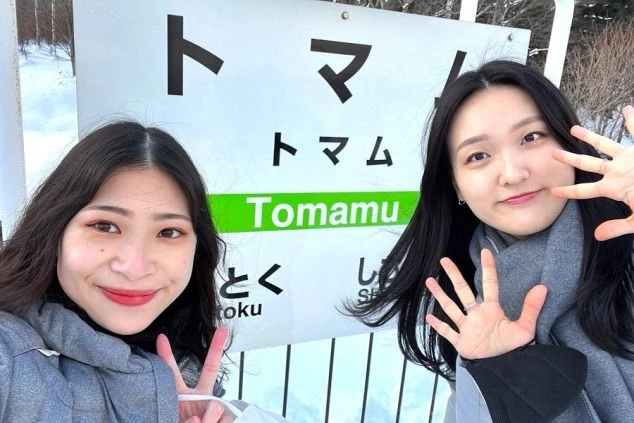 「トマム」駅の看板の前でピースサインをする2人の女性。冬のトマムでのリゾートバイトの様子。