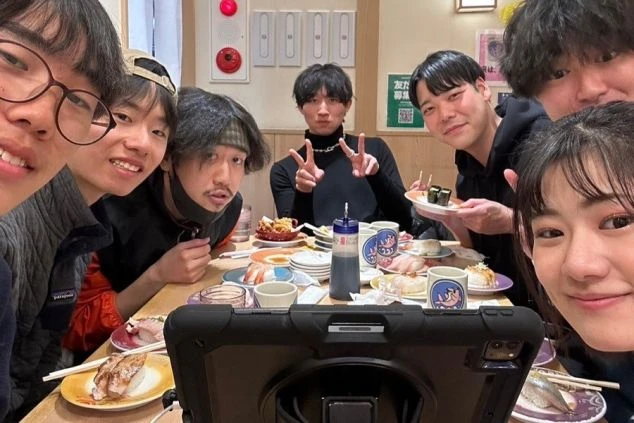 回転寿司店で食事を楽しむ若者グループ。リゾートバイトの仲間との楽しいひととき。