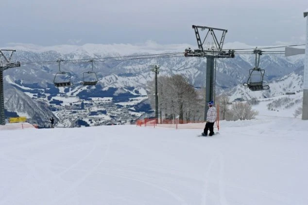 スキー場のゲレンデから雪に覆われた街並みと山々を見下ろすスノーボーダーが映るイメージ画像。リゾートバイトの休日を満喫。