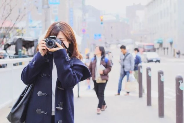 街中でカメラを構え、写真を撮る女性。リゾートバイトのオフの日の過ごし方のイメージ。