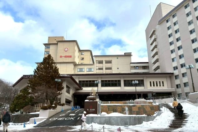 雪景色と噴煙が上がる登別地獄谷の絶景。手前には「登別地獄谷」と書かれた看板と柵が見える。