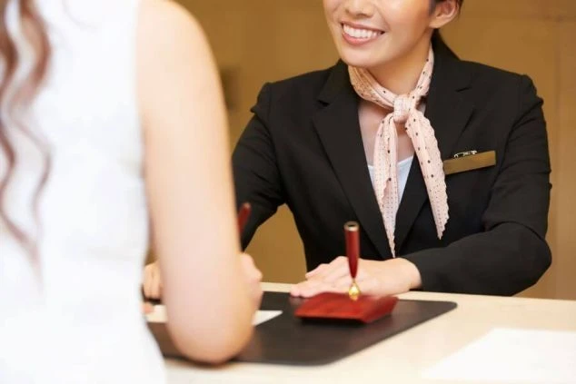 ホテルのフロントで笑顔で顧客対応をする女性スタッフ。お辞儀をする姿勢から丁寧な接客が伺え、リゾートバイトでホテルや旅館のフロント業務に興味がある方に訴求する画像。