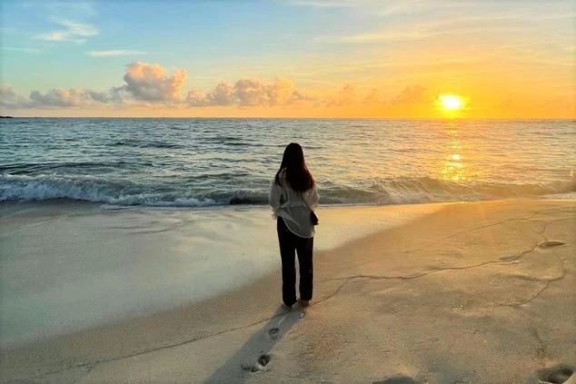 夕焼けのビーチに立つ人物の後ろ姿が映るイメージ画像。波打ち際に足跡が残り、リゾートバイトの休日を満喫。