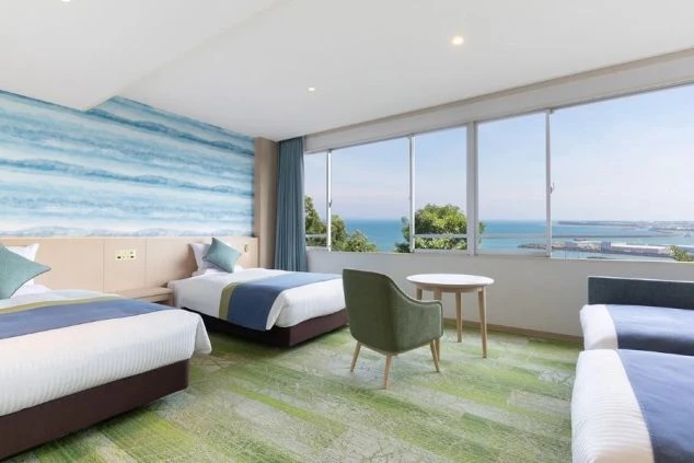 海が一望できるホテルの客室。ベッド2台、ソファ、テーブルが置かれ、窓から港と海が見える職場のイメージ画像。