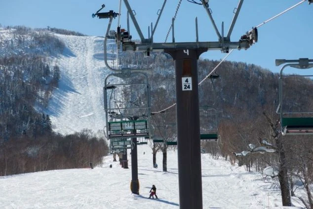 青空の下、雪山に設置されたスキーリフトと、その下のゲレンデを滑るスキーヤー。リゾートバイトでリフトスタッフやゲレンデ整備の仕事に興味がある方に訴求するワクトリオリジナル画像。
