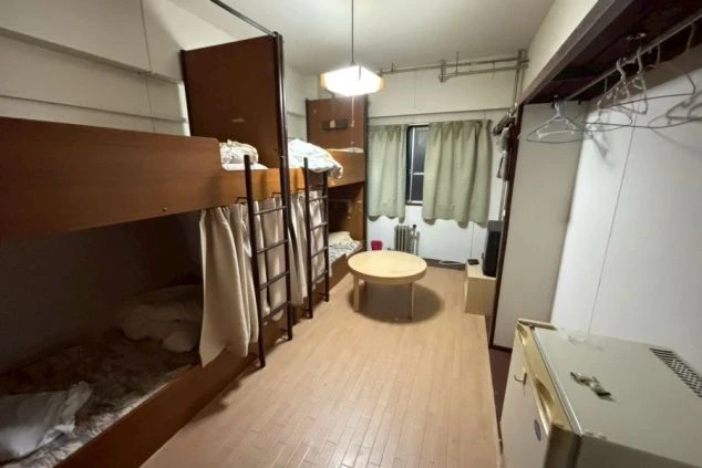 リゾートバイトの相部屋寮写真。二段ベッドが2台設置された4人部屋。ミニ冷蔵庫、丸テーブル、テレビ、クローゼット(ハンガー)など、共同生活に必要な家具家電が揃っている。