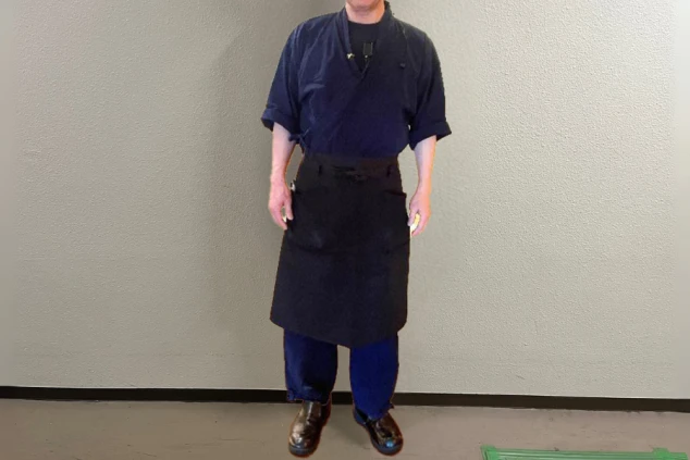 紺色の作務衣風の上着とパンツ、黒い前掛けを着用した男性スタッフの和風の制服画像。