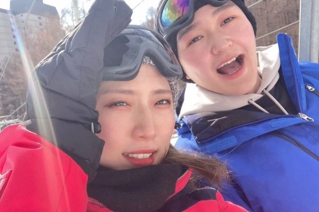 スキー場でリフトに乗り、笑顔で自撮りをする2人の若者。ウィンタースポーツを楽しむリゾートバイトのイメージ。