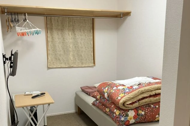 リゾートバイトの寮の部屋の中を撮影した画像。壁にテレビが取り付けられており、洗濯物が干せるハンガーラックも備え付けられている。リゾートバイトの寮の部屋の画像。