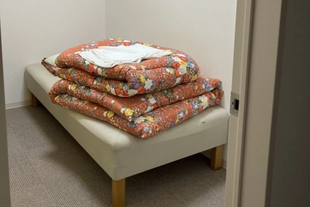 リゾートバイトの寮の部屋の中を撮影した画像。小さなベッドに布団が畳んで置かれており、床は絨毯(じゅうたん)敷きである。リゾートバイトの寮の部屋の画像。