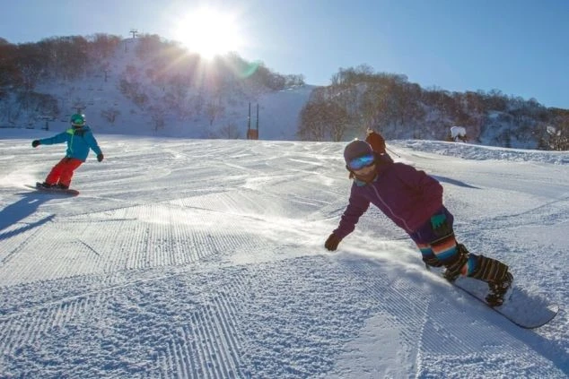 スキー場で滑走するスノーボーダーたちの画像。青い空と太陽の光が降り注ぐ中、雪煙を上げながらターンをしている。リゾートバイトの休日にウィンタースポーツを満喫できる。