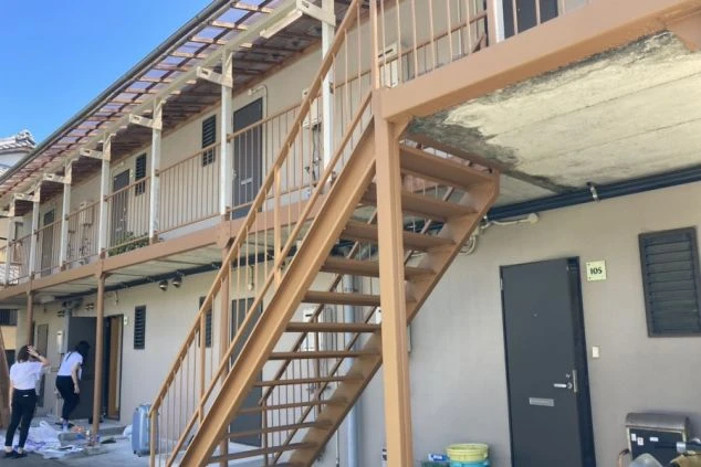 2階建ての寮の外観。屋外に鉄製の階段があり、各部屋の扉が並ぶ廊下には屋根が設置されています。