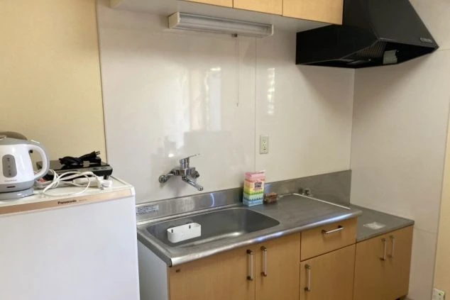 寮のキッチン。木目調の収納扉がある流し台に、電気ケトルやIHクッキングヒーターが置かれています。