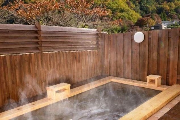 旅館にある、こじんまりとした木製の露天風呂。湯気が出ており、紅葉を背景に温泉を楽しめる。