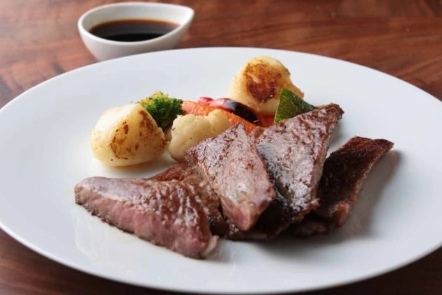 白い皿に美しく盛り付けられたステーキと温野菜のイメージ画像。ホテルで提供される食事。