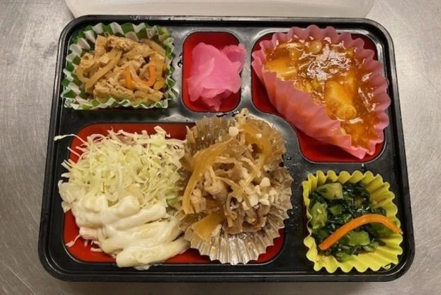 様々な種類のおかずが詰まったお弁当。肉じゃが、マカロニサラダ、お漬物など