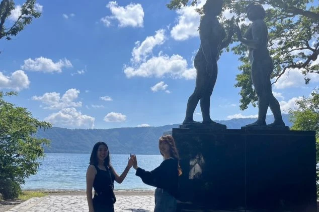 ワクトリでリゾートバイトをしたスタッフが撮影した、十和田湖畔の乙女の像とポーズをとる女性二人のイメージ画像。リゾートバイトの休日を満喫。