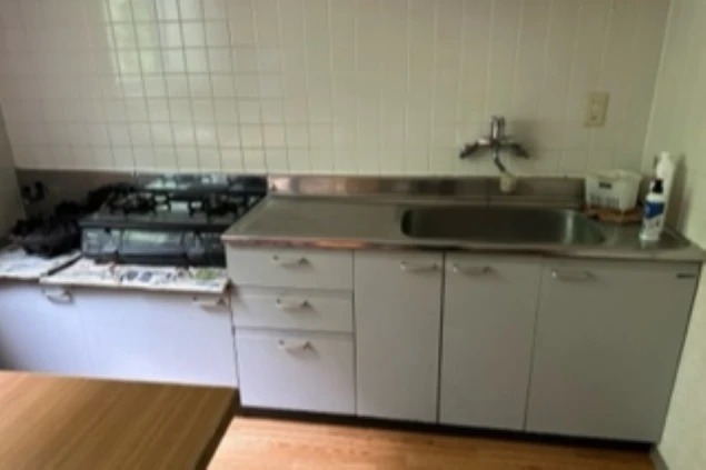 リゾートバイトの寮のキッチン。シンクとガスコンロ、白いタイル、調理台下の収納が映る。