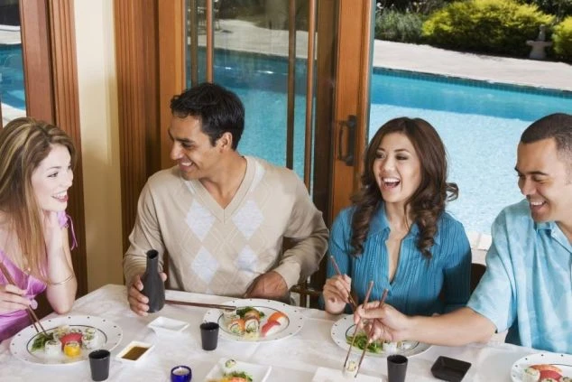 プールが見えるレストランで食事を楽しむ外国人4人の人々。海外客が多いホテルのイメージ。