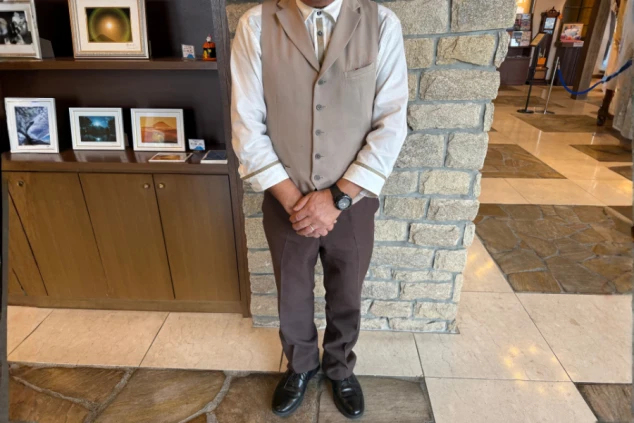 リゾートバイトのフロントスタッフ男性の制服画像。ベージュのベストと白シャツ、茶色のパンツの組み合わせで、上品で格式あるホテルの受付にふさわしい服装。