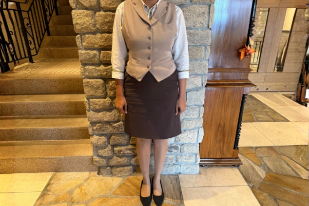 リゾートバイトのフロントスタッフ女性の制服画像。ベージュのベストと茶色のスカート、白シャツの組み合わせで、洗練された雰囲気のホテル勤務に最適な服装。
