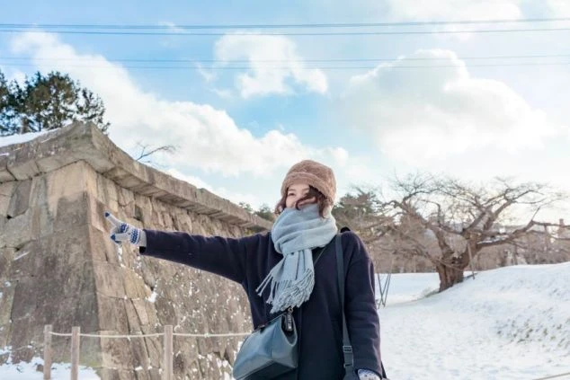 雪が積もった場所で、笑顔の女性がポーズをとるイメージ画像。リゾートバイトの休日を満喫。