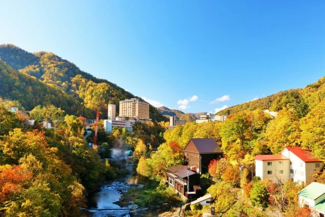 紅葉の渓谷に温泉街が広がる秋の絶景のイメージ画像。リゾートバイトの休日を満喫。