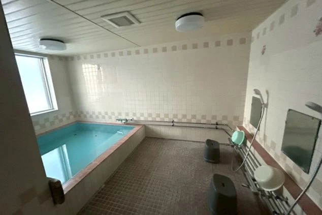 寮の洗面所。洗面台と棚、洗濯機が映り、カゴが置かれた共用スペース。