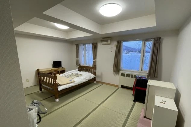 寮の個室。ベッド、テレビ、冷蔵庫、机、クローゼット、暖房器具が映る。