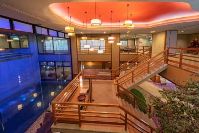 和風モダンの内装が特徴的な旅館のロビーと階段。天井からは複数の照明が吊り下がり、豪華な雰囲気が漂う、リゾートバイトでホテルや旅館のスタッフとして働くイメージが伝わる画像。