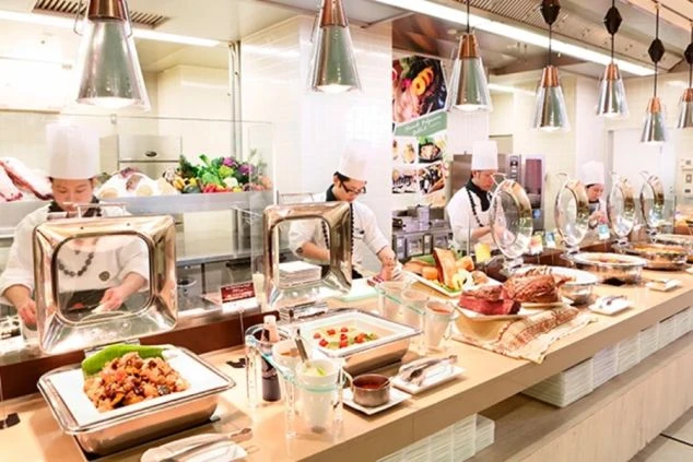 リゾートバイトの勤務先の活気あるビュッフェレストランのキッチンカウンターの様子。シェフが目の前で調理しており、党利補助業務で行うライブキッチン業務のイメージ。