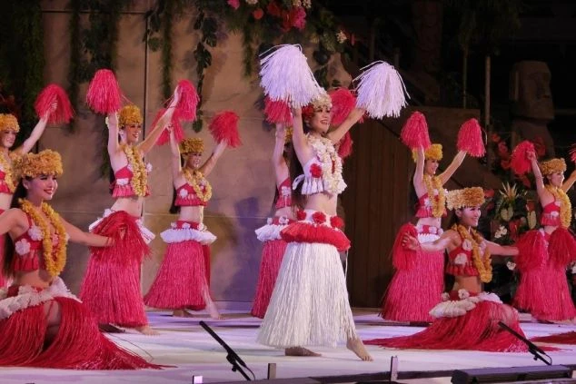 ハワイアン衣装を身につけ、ポンポンを持って笑顔で踊る女性たち。スパリゾートハワイアンズのショーの様子。