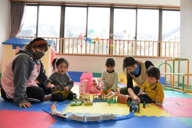 野沢温泉の託児所の画像。広々とした室内で、子供たちが保育士と一緒に電車のおもちゃで遊んでいる。リゾートバイトの勤務ちなか
