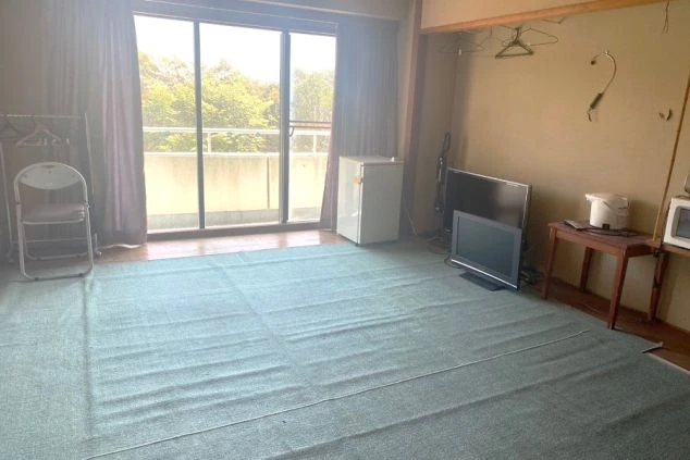 リゾートバイトの個室寮の広々とした室内。バルコニーに面した窓から光が差し込み、ミニ冷蔵庫やテレビ、ハンガーラックが備え付けられた、快適な寮画像。