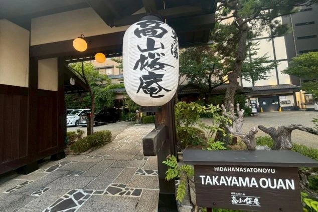 「高山桜庵」の提灯が掛かった門を正面から捉えた写真。門の奥には緑の植栽とホテル棟が見え、和とモダンが調和している。