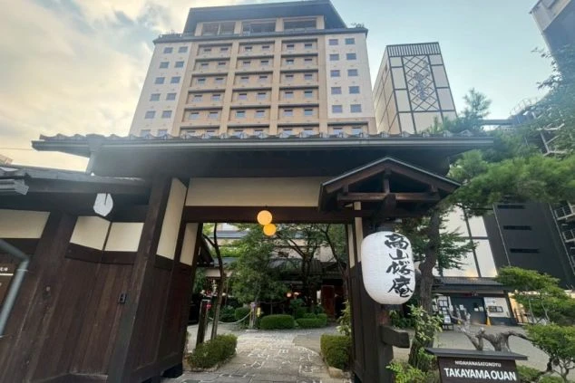 和風の門から奥の庭と高層のホテル棟を見上げるアングル。提灯が吊り下げられた門の向こうに、モダンな建物が広がる。