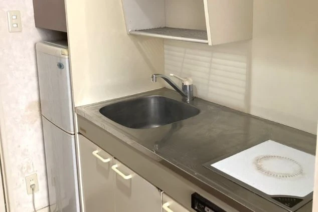 寮のキッチン。シンクとコンロ、冷蔵庫、洗濯機、吊り戸棚が備え付けられた空間が映る。
