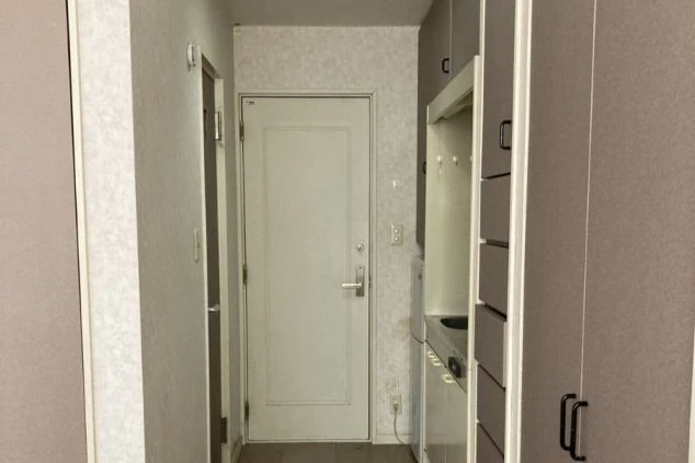 寮の玄関。扉の奥に部屋へ続く空間。右側にキッチンと収納棚が映る。