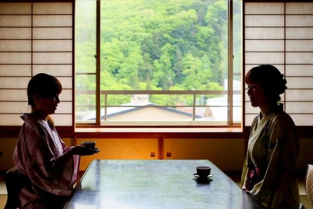 旅館の客室で向かい合う2人の女性の画像。窓の外には緑豊かな景色が広がり、和の趣を感じさせる空間。