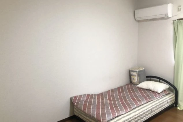 アパート寮の部屋の中の画像。ベッドが一つ置かれ、エアコンも見える。